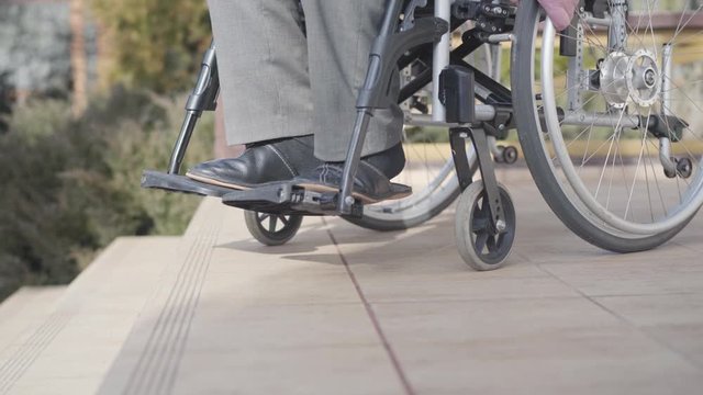 Side view close-up of wheelchair with unrecognizable old man rolling to stairs. Concept of ramp availability, disability challenges, lifestyle.