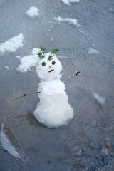snowman in puddle. bad warm rainy winter weather. melted snowman. anomaly weather concept. close up. 