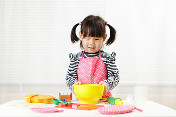 toddler girl pretend play food preparing role at home agianst white background
