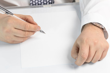 businessman writes on a sheet of white paper. Dressed in a shirt and tie. Close-up