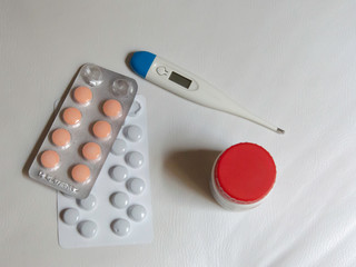 packs of medicine blisters, a red pack pill and a thermometer on a white background