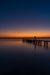 A man silhouette standing on wooden pier lonely at the sea with beautifulsunset. lsunset seascape at a wooden jetty