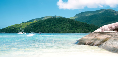 Beautiful seascape bay with luxury yachts at the coast, tropical island at background and crystal blue water at foreground