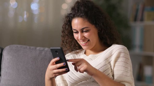 Happy arab woman using smart phone sitting on a couch at home in the night