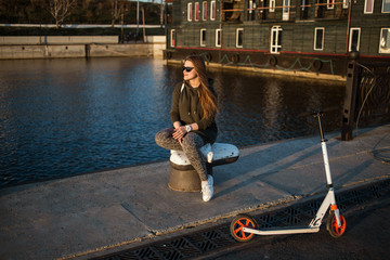 Happy girl relaxing with kick scooter on warm spring evening.