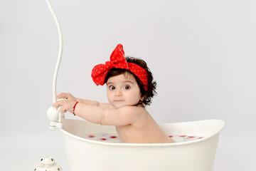 Cute adorable baby girl having milk bath with strawberries. Girl eating strawberries on white background	