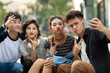 Happy young Chinese friends taking selfie with smartphone