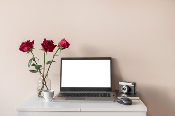 Home office or blogger concept, mockup. Laptop with white isolated screen, flowers, retro camera on white table on neutral background