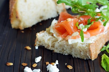 Sandwich with slightly salted salmon, arugula, seeds and cottage cheese on the board. Sourdough bread toast with salted fish, smorrebrod.