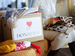 Closeup on donation box and woman packing clothes in background - Powered by Adobe