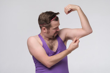 Funny weak sportsman exercising looking on his biceps.
