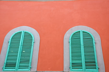 Green wodden windows on an orange wall in Italy