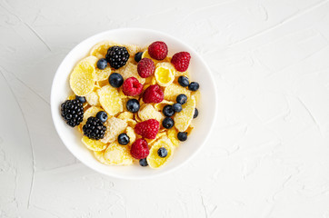 Healthy breakfast with cornflakes in a white plate, berries, milk and coffee on a white background.
