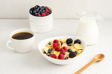 Healthy breakfast with cornflakes in a white plate, berries, milk and coffee on a white background.