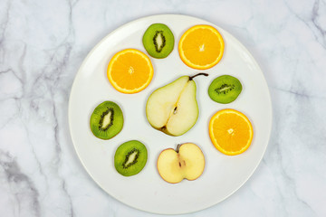 sliced fruits pear kiwi orange apple on a white plate with minimalist marble background