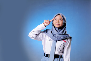 Fototapeta premium a Muslim high schoolgirl student shows gesture thinking by putting her finger on her head isolated on blue background