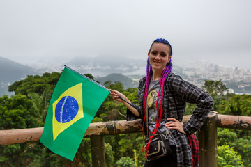 A girl with purple braids on her head waving a Brazilian flag.