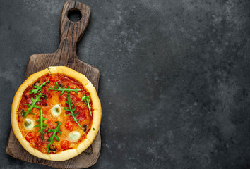  tasty italian pizza with tomatoes, cheese, quail eggs, sausage on a cutting board on a stone background with copy space for your text