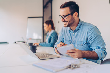 Young businessman writing notes during video call