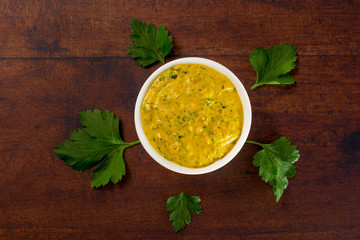 Vegan tahini sauce with garlic, turmeric and  minced parsley leaves, in a white bowl, surrounded...