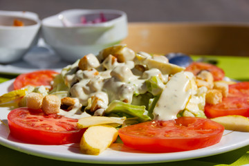 Delicious tomato salad with croutons, lettuce, apple and caesar dressing on top. Healthy vegetarian meal close up. Vegetables and fruit mix meal