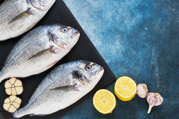 Fresh Royal Dorada on blue backdrop with lemon and garlic. Healthy food concept. Top view, copy space. Mediterranean seafood concept
