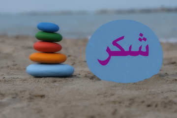 Thank you in arabic language with a creative stones composition on the beach