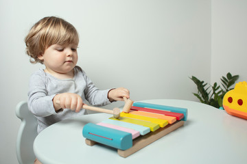 Beautiful toddler play with a  xylophone toy at home. Happy child play at the table in the baby room. Child plays musical instrument. Funny baby. Play music. Lifestyle.