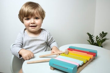 Beautiful toddler play with a  xylophone toy at home. Happy child play at the table in the baby room. Child plays musical instrument. Funny baby. Play music. Lifestyle.