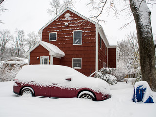 red car in front of red suburban house during the snow storm