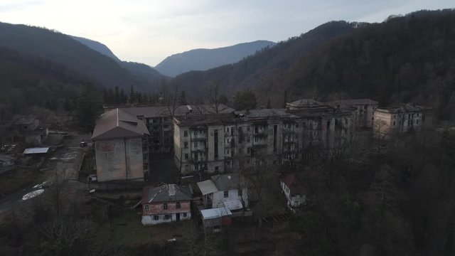 Old settlement at the top of mountain hill. Shot. Aerial view of the old abandoned residential buildings surrounded by mountains with trees.
