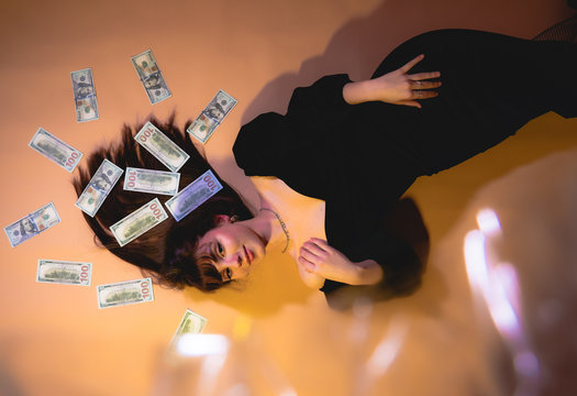 Business concept. Saving money concept. Business success concept. Digital money concept. Finance. Beautiful girl lying in money. Woman in elegant black dress lying in banknotes.