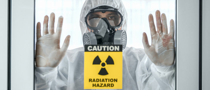 scientist with coverall protection clothing and full face protection mask in control room with radiation hazard sign