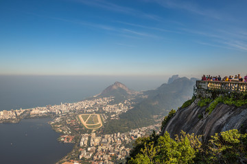 Tourists enjoying aerial view from Christ the Redeemer overlooking Rio with views of Gavea, Leblon & Jockey Club Brasileiro on clear sunny day with blue sky