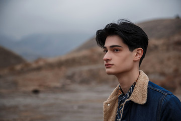 Dramatic portrait of a young brunette guy in cloudy weather against the background of mountains