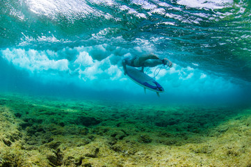 Fototapeta na wymiar Surfer duckdiving a wave over a shallow coral reef