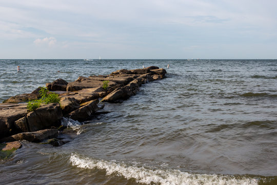 A rocky road among the lake.  Summer landscape with a lake, waves breaking on the shore and a blue cloudless sky.