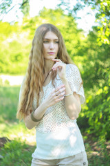 Portrait of a woman wearing a white knitted blouse and beige shorts on nature on a summer day.