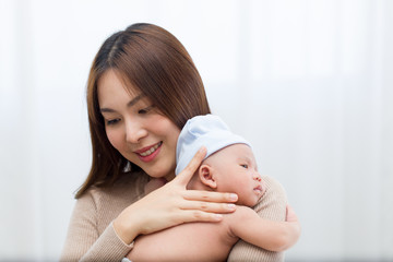 Beautiful mom holding a newborn baby and tenderly cuddles gently while the infant is sleepy on the shoulder. Asian young mother tries to lull her child to sleep with love and care.