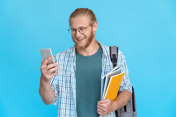 Bearded pleased young man student hipster blogger glasses hold modern smart phone smile at screen...