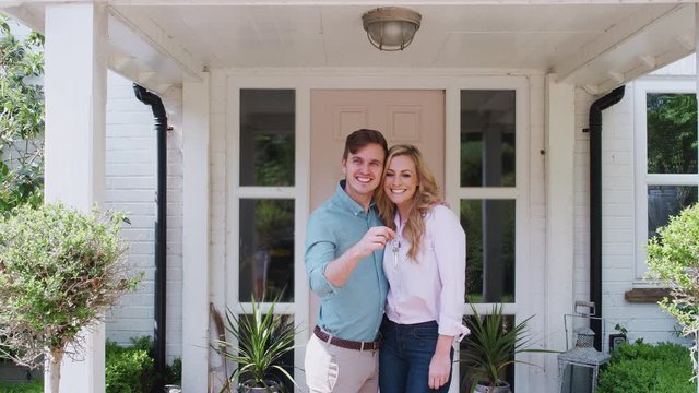 Portrait Of Couple Holding Keys To New Home Standing Outside Front Door