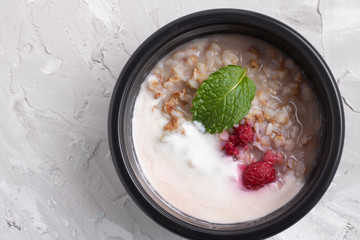 Boiled buckwheat porridge with strawberry in a black container, top view and copy space