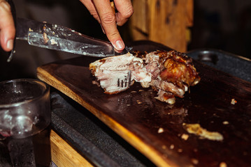 Chef hand cuts piece grilled pork in steaks with knife. Traditional suckling pig cooked on the...