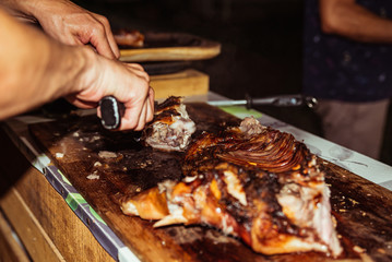 Chef hand cuts piece grilled pork in steaks with knife. Traditional suckling pig cooked on the...