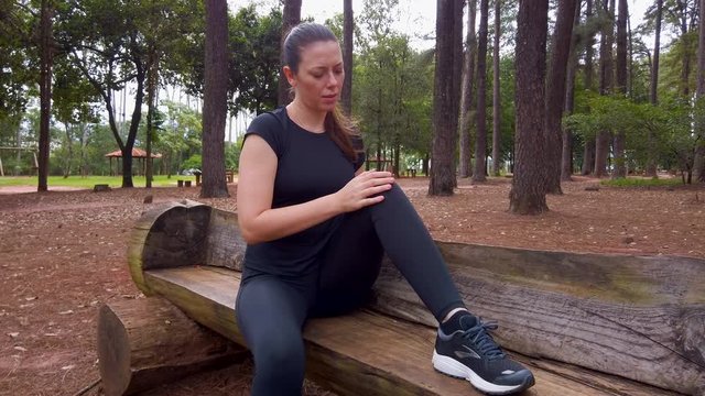 Athlete woman in ache palpating the knee joint. Camera moving from her front to the side.