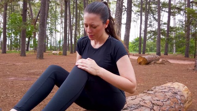 Athlete woman at a forest garden suffering with aching knee, palpating the joint.