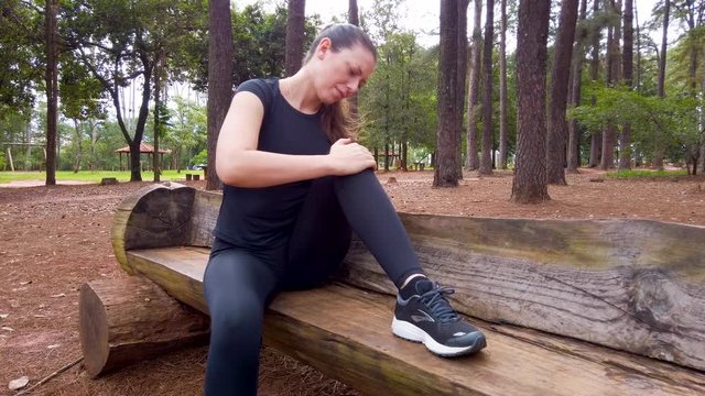 Athlete woman massaging her own leg. Aching knee joint. Forest garden.