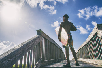 Young teen on sunny bridge carrying a surfboard