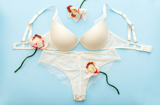 Bra and pantie. White lace lingerie on blue background. Flat lay with lace underwear. Beautiful romantic sexy passion full coverage bra. Set of white bra and erotic bikini with flowers pink orchid.