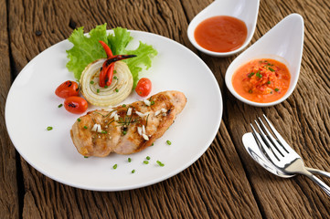 Grilled chicken on a white plate with tomatoes, salad, onion, chili and sauce.